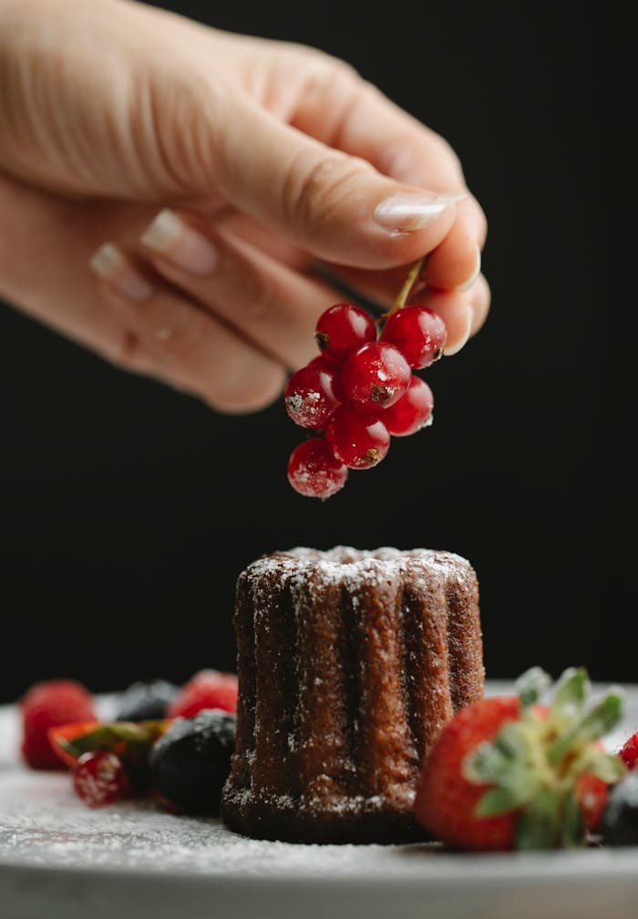 Crop faceless woman decorating cake with currant